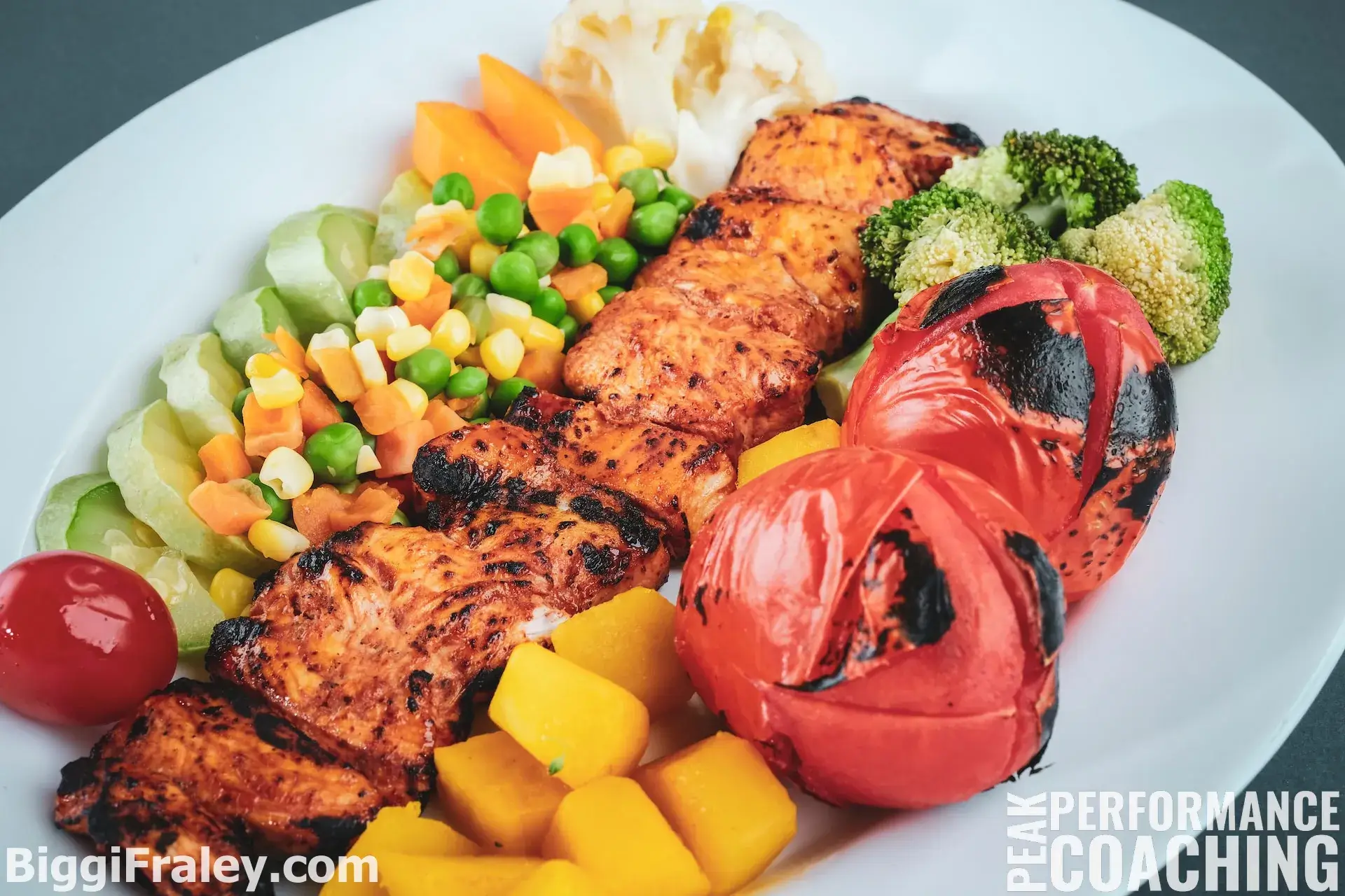 white plate with beautifully arranged grilled chicken, mixed vegetables and tomatoes