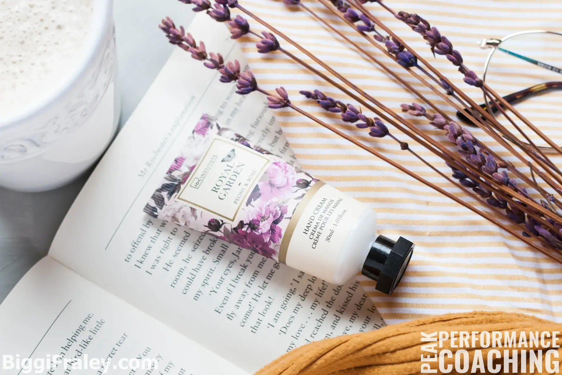 lavender, a cup of coffee, a book, hand cream, and a pair of glasses on a table